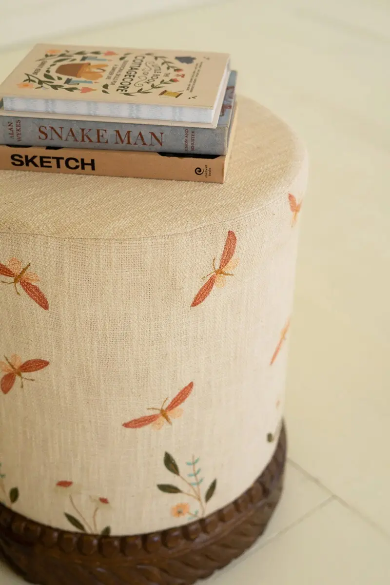 Cream Upholstered Ottoman Featuring Carved Wooden Base And Decorative Detailing 1